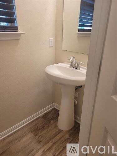 A white pedestal sink in a bathroom with wooden flooring and a mirror above it.