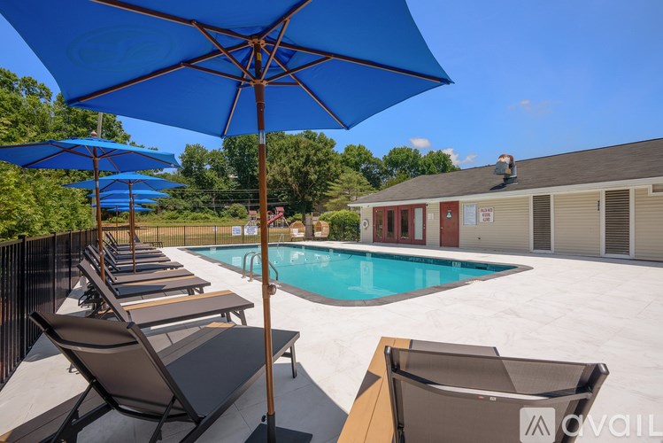 A row of lounge chairs are set up under blue umbrellas by a pool.