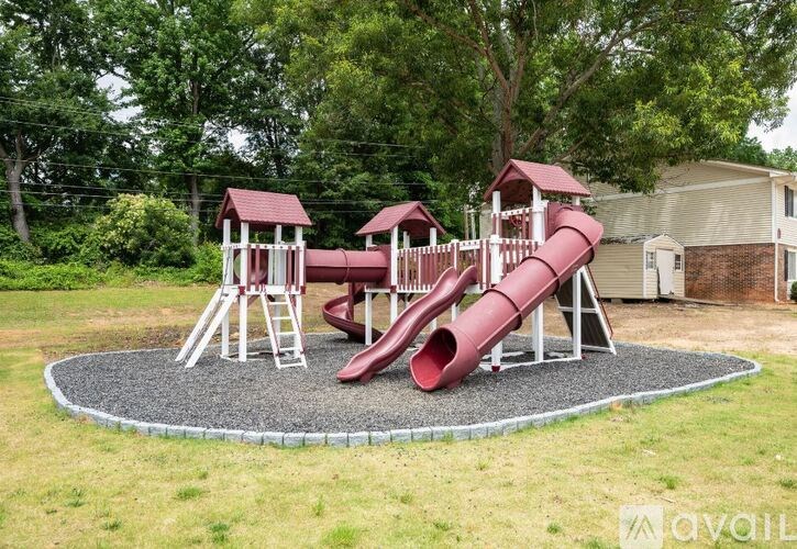 A playground with a red slide and two red swings.