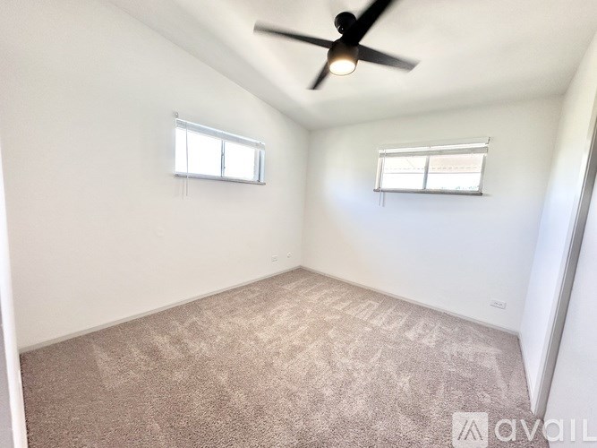 A room with a ceiling fan and two windows.