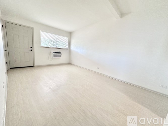 A spacious room with light wood flooring and a window with blinds.