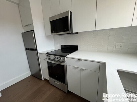 A kitchen with white cabinets and a black microwave above the stove.
