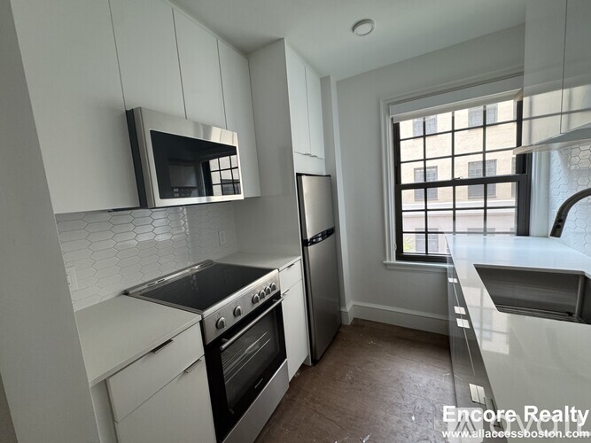 A kitchen with white cabinets and a black microwave.
