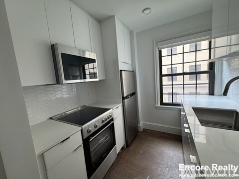 A kitchen with white cabinets and a black microwave.