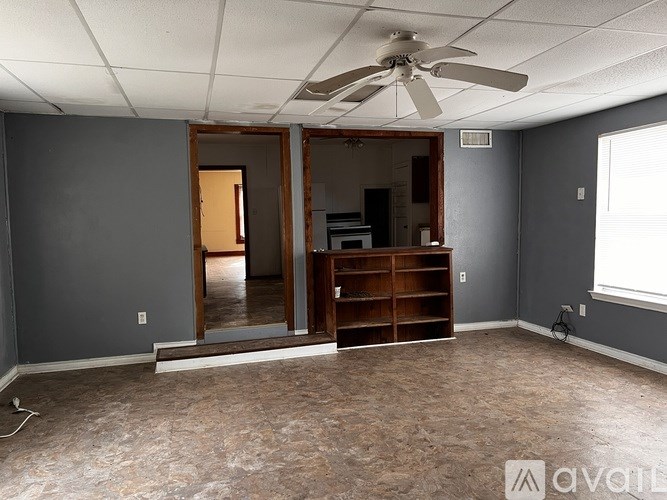 A room with a ceiling fan and a large open door leading to another room.
