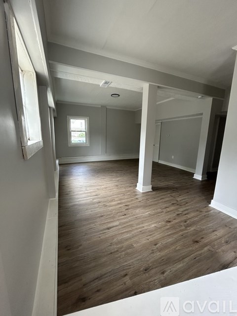 A room with wooden floors and white walls, with a window and a door visible.