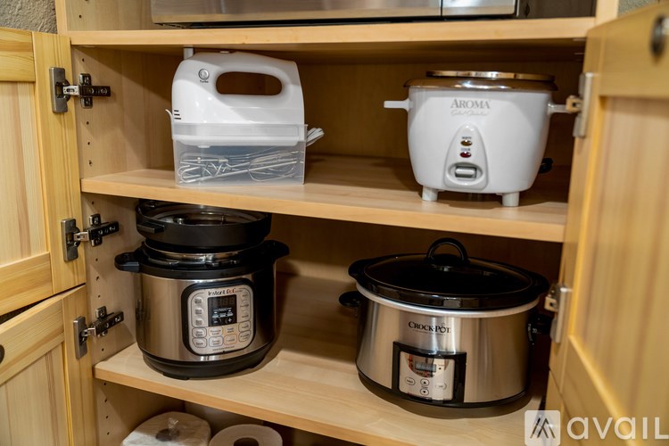 A kitchen cabinet with a rice cooker and a slow cooker on the shelf.