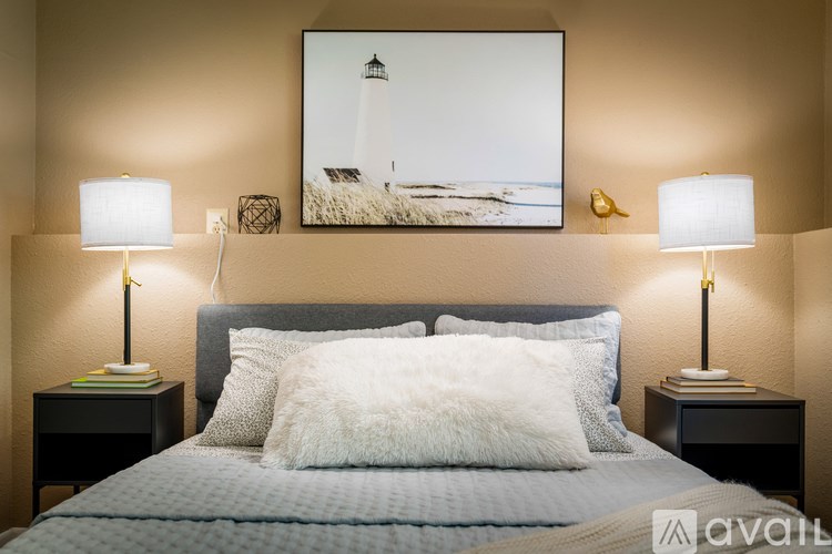 A bedroom with a bed, two lamps, and a picture of a lighthouse on the wall.