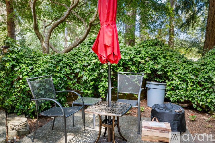 A patio with a table, chairs and a red umbrella.