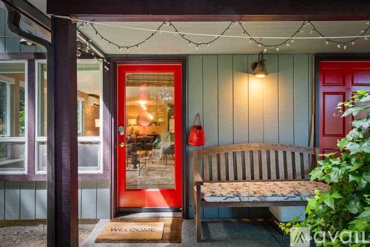 A wooden bench sits in front of a red door on a porch.