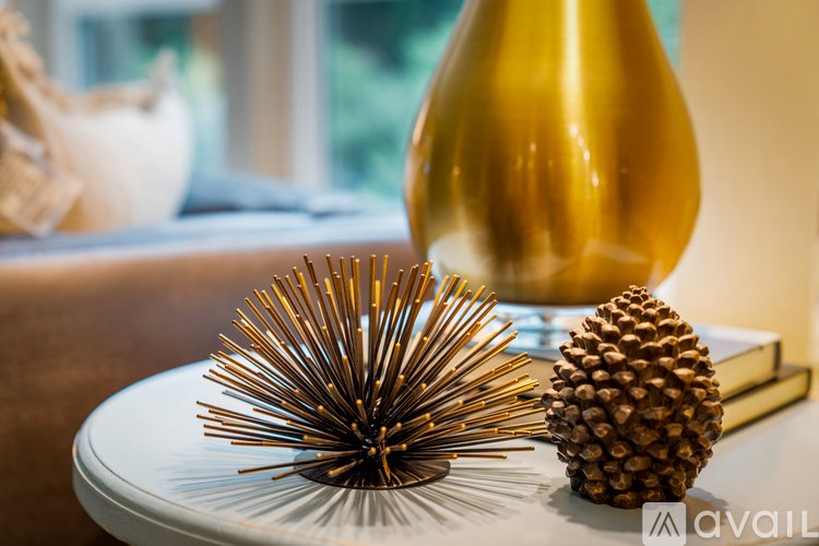 A golden vase sits on a table next to a white teapot and a brown pine cone.