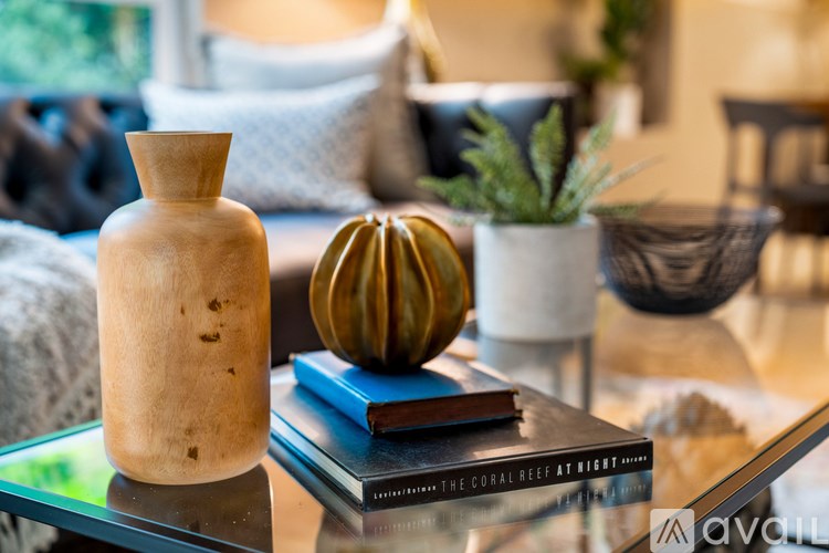 A wooden vase sits on a glass table next to a stack of books and a small potted plant.