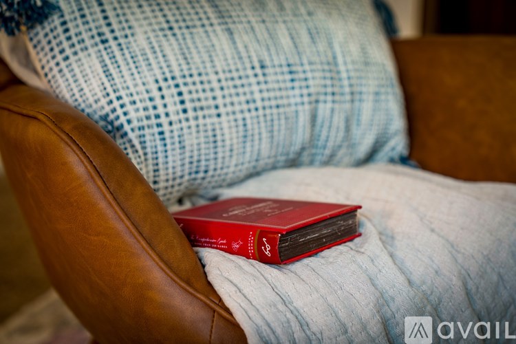 A red book sits on a pillow on a brown leather chair.