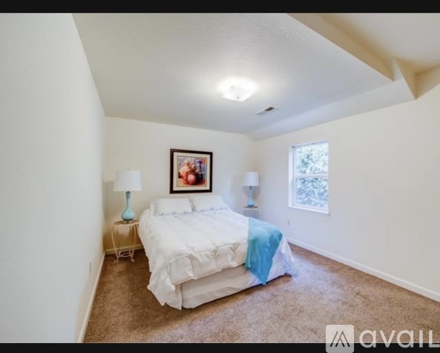 A bedroom with a bed, two lamps, and a picture on the wall.