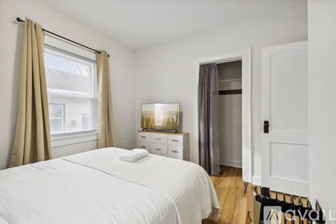 A bedroom with a white bed and a window with beige curtains.