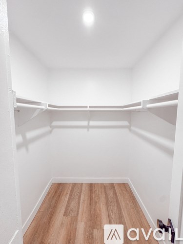 A white walk in closet with wooden floors and shelves.