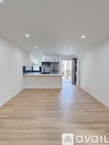 A spacious kitchen with wooden flooring and white walls.