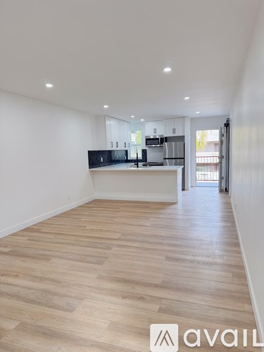 A spacious kitchen with wooden flooring and white walls.