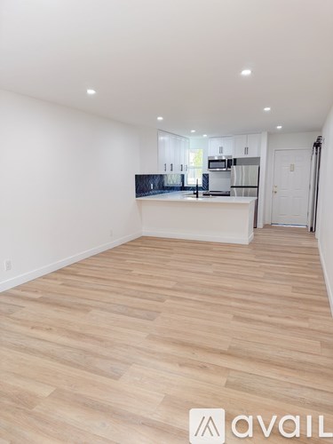 A spacious room with wooden flooring and a kitchen area in the background.