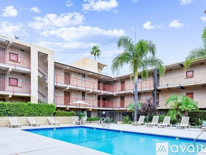 A large swimming pool is surrounded by lounge chairs and palm trees in front of apartment buildings.
