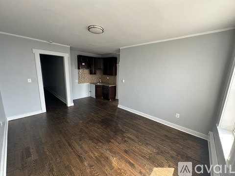 A room with wooden flooring and a kitchenette in the background.