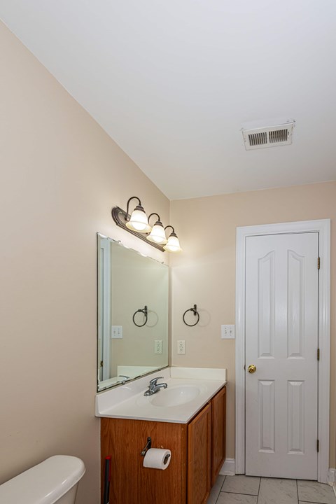 A bathroom with a white door, a mirror, and lights above the mirror.