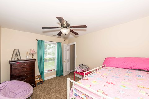 A bedroom with a pink bed and a ceiling fan.