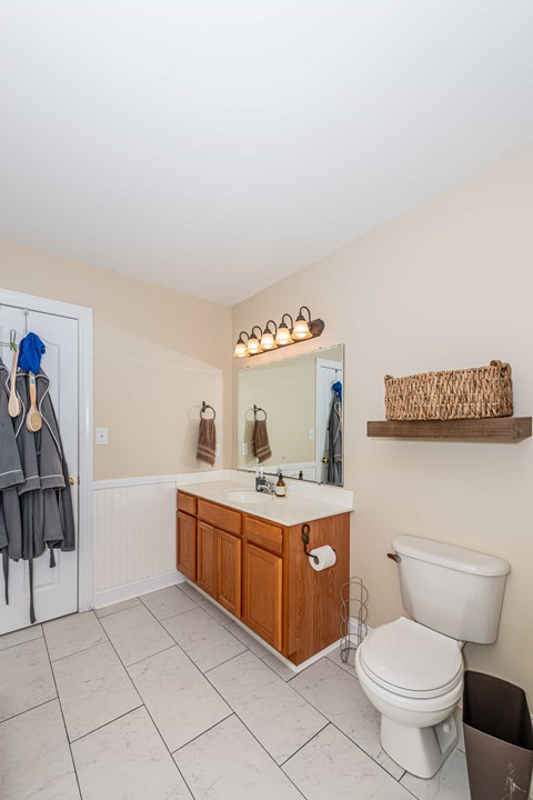 A bathroom with a white toilet, a sink with a mirror above it, and a towel rack with two towels hanging on it.