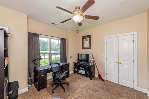 A room with a desk, chair, and a fan.