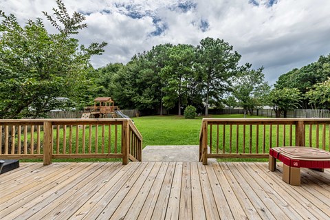 A wooden deck with a bench and a tree in the background.