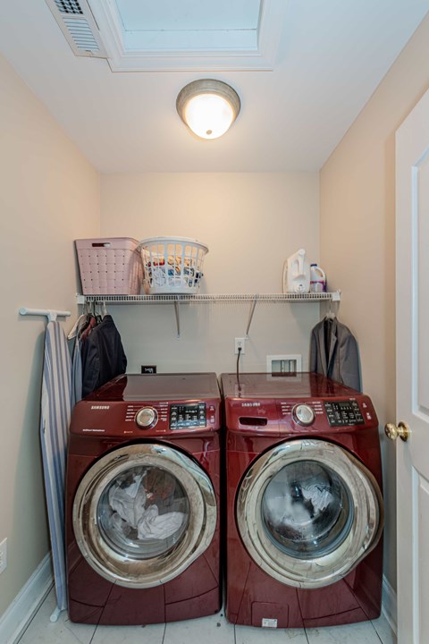 Two red front load washing machines in a laundry room.
