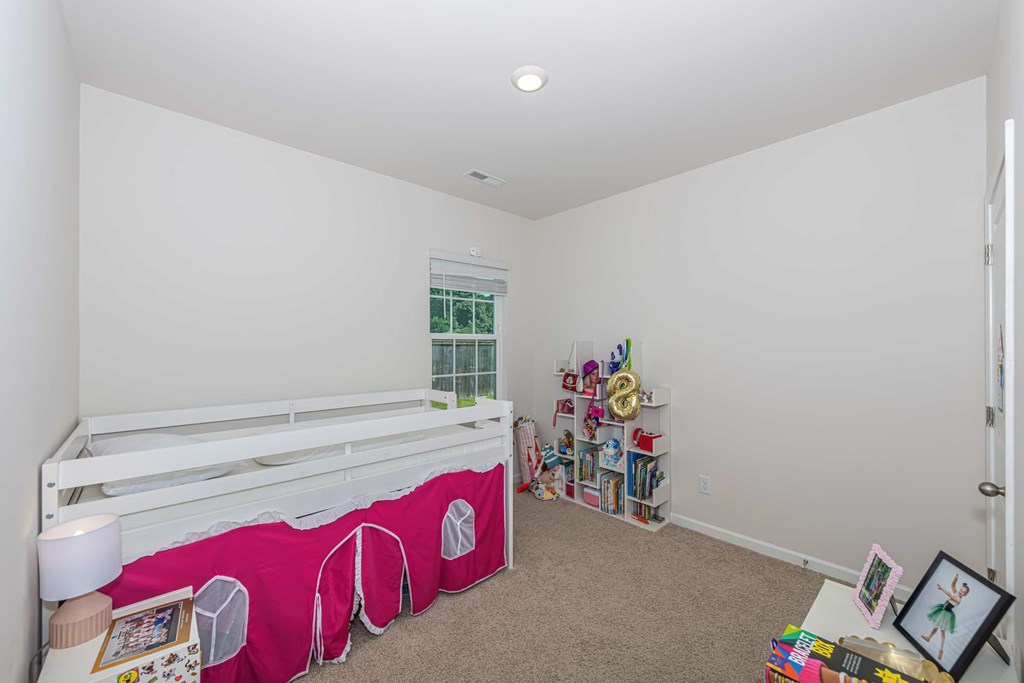 A white bed with a pink blanket and a white shelf with various items on it.