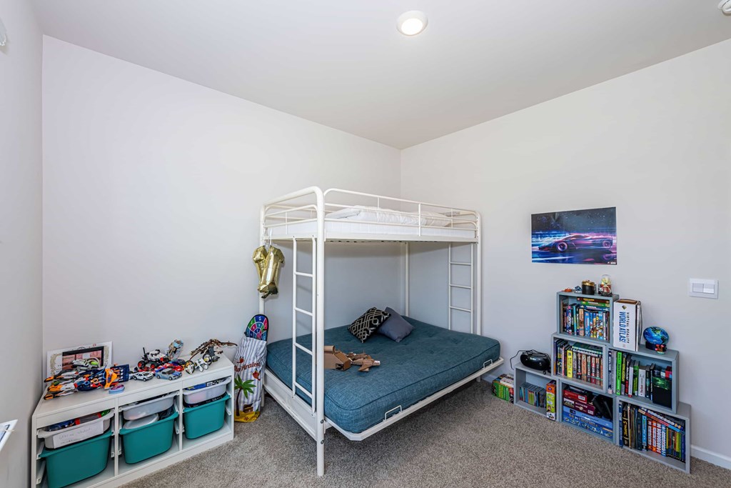 A white bunk bed with a blue mattress is in a room with a bookshelf and a poster on the wall.