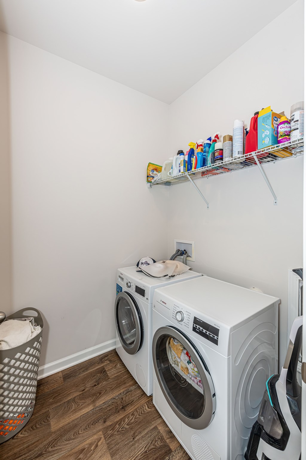 A white washing machine sits in a laundry room next to a shelf with cleaning supplies.
