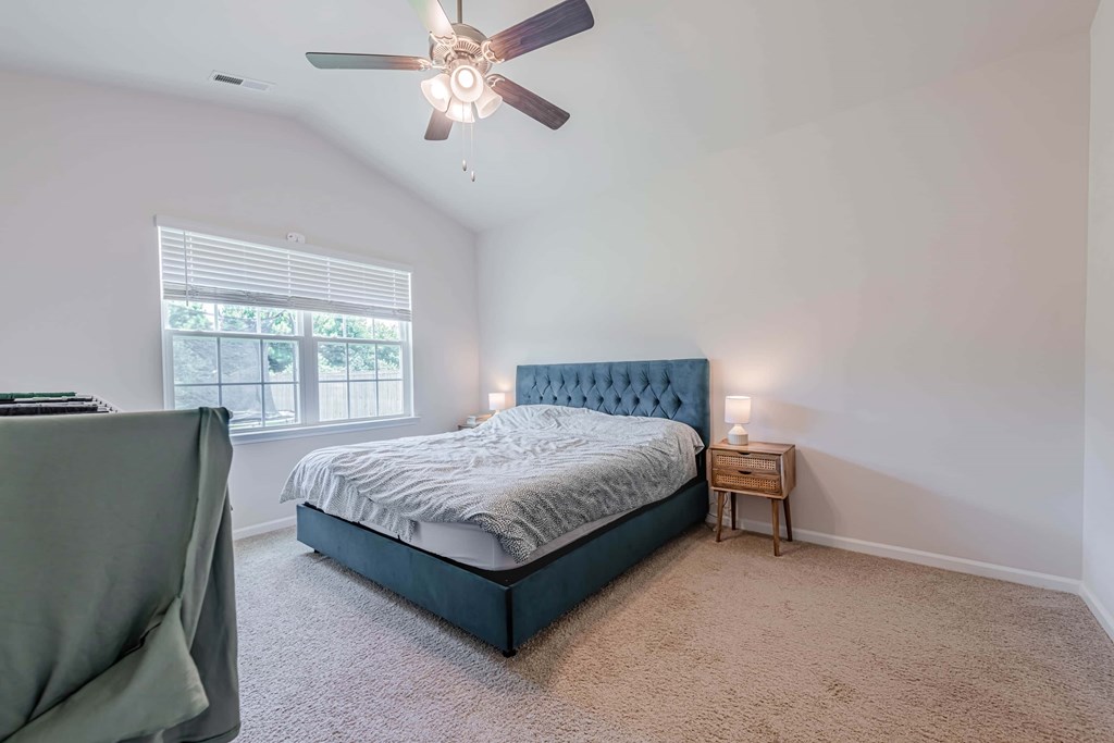 A bedroom with a bed, a chair, and a ceiling fan.