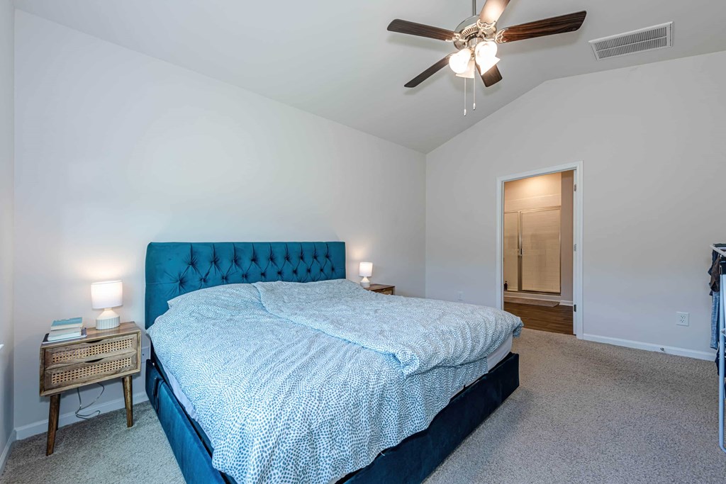A bedroom with a blue bedspread and a ceiling fan.