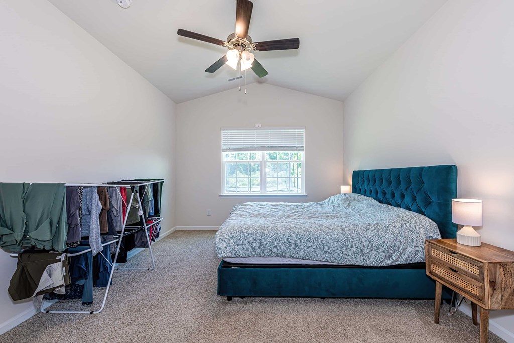 A bedroom with a bed, a ceiling fan, and a window.
