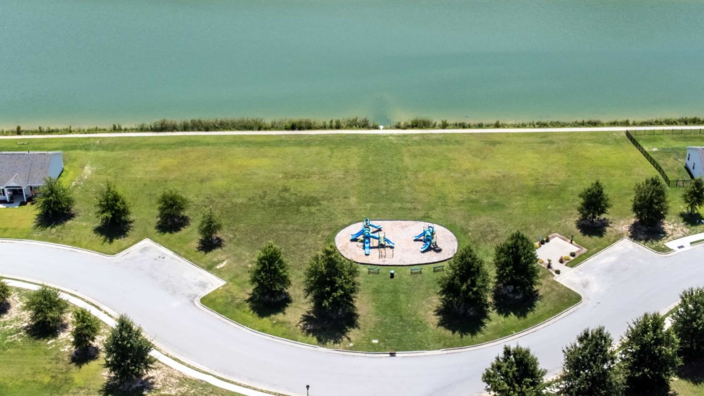 A playground with a blue slide is surrounded by a white fence and trees.