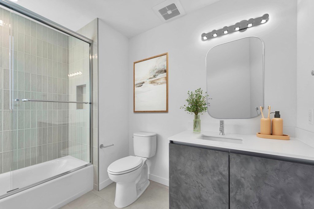 A modern bathroom with a white toilet, a glass shower, and a grey counter.