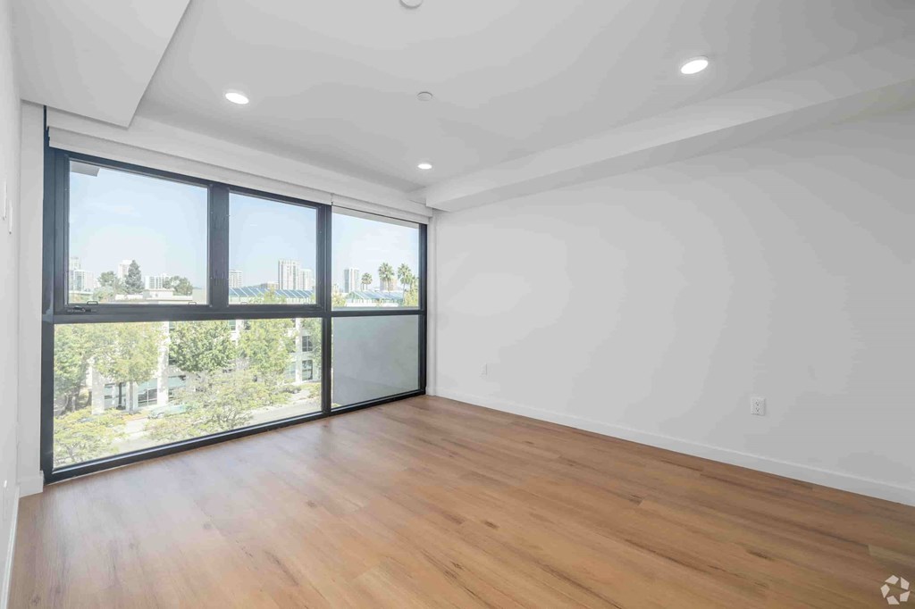 A room with wooden flooring and large windows overlooking a cityscape.