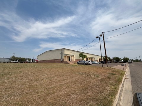 A large building with a grey roof is situated in a grassy area with a road in front of it.