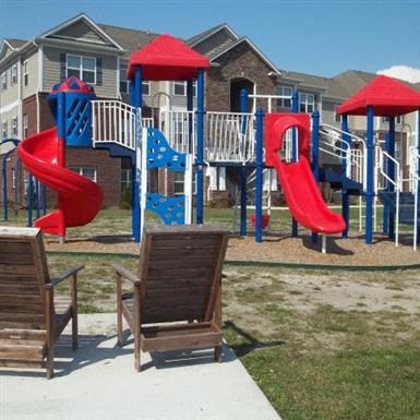 a playground with slides and chairs in front of an apartment building