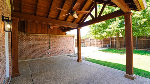 A covered patio area with a ceiling fan and brick wall.