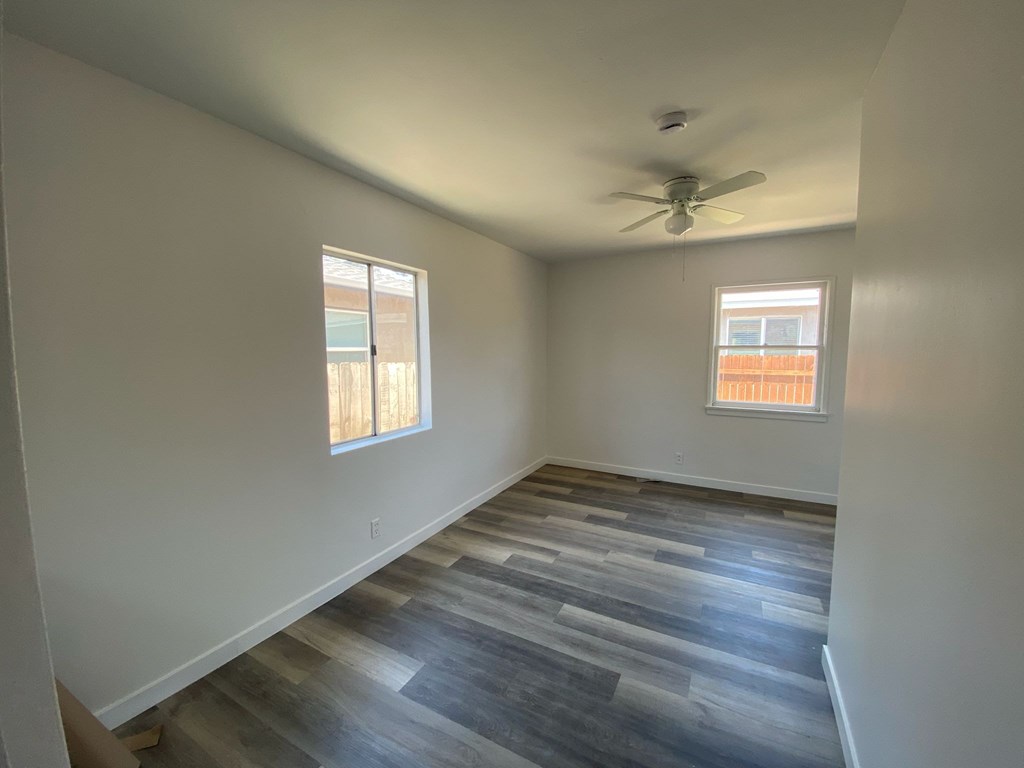 A room with a ceiling fan and two windows.