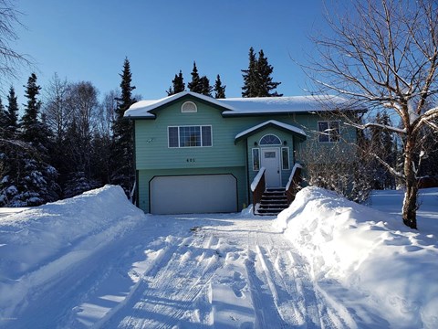A house with a green exterior is surrounded by snow.