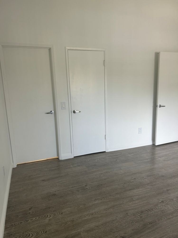 Three white doors are closed in a room with wood flooring.