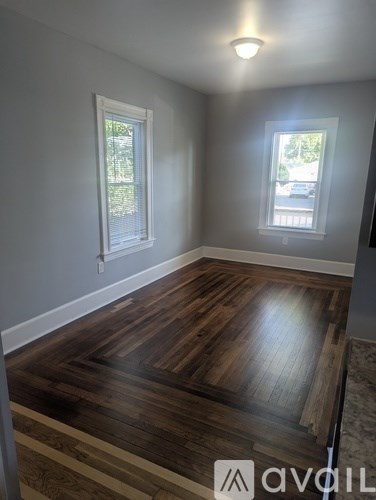 A room with wooden flooring and two windows.
