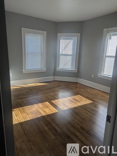 A room with wooden flooring and two windows.