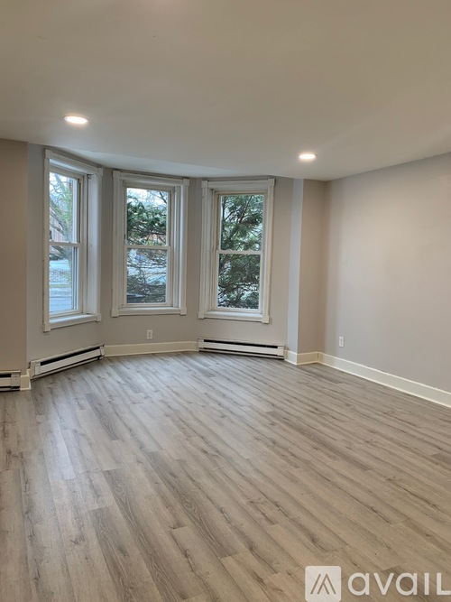 A room with wooden flooring and three windows.