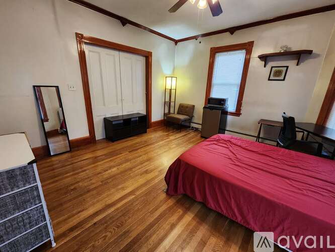 A bedroom with a red bedspread and wooden floors.
